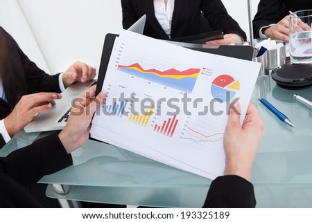 Cropped image of businesswoman holding financial progress chart at desk in office