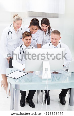 Team of doctors using desktop PC together at desk in clinic