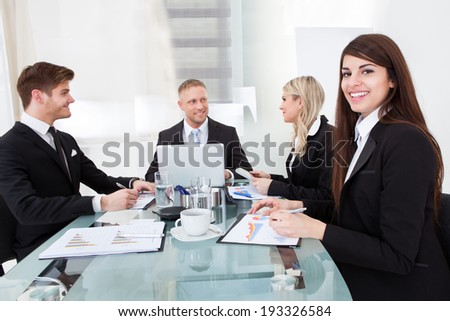 Portrait of smiling businesswoman sitting with colleagues in meeting at office