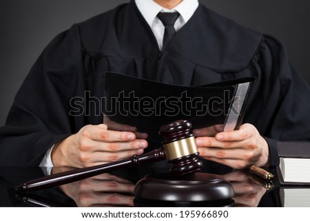 Midsection of male judge holding file with mallet on desk against black background