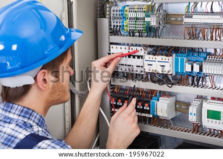 Side view of male technician examining fusebox with multimeter probe