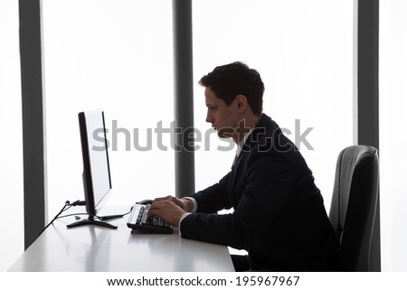 Side view of young businessman using computer at desk in office