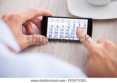 Closeup of businessman touching calendar date on mobile phone in office