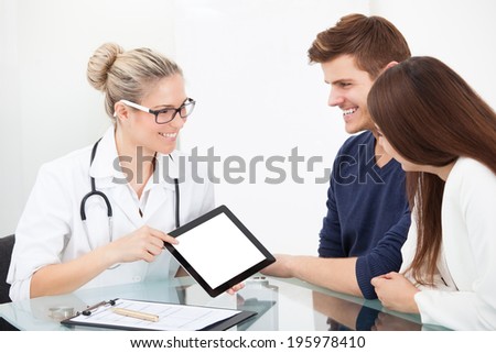 Female doctor showing medical report to couple on digital tablet at clinic