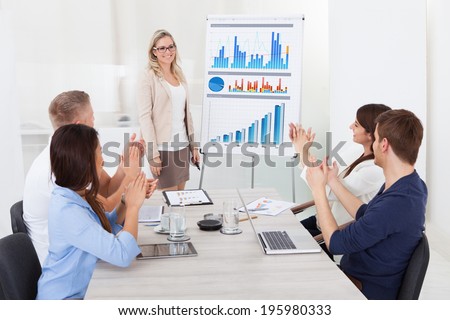 Young businesspeople clapping for female colleague after presentation at desk in office