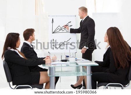 Businessman writing on flipchart while giving presentation to colleagues in office