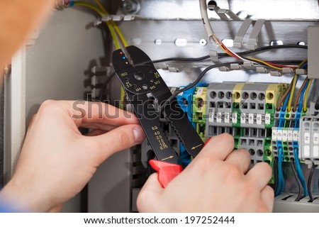 Closeup of male technician cutting cable with fusebox in background