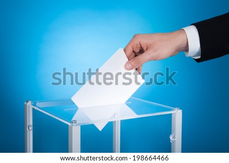 Cropped image of businessman putting paper in election box against blue background