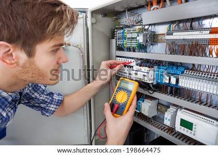 Side view of male technician examining fusebox with digital insulation resistance tester
