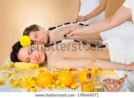 Relaxed young couple receiving hot stone therapy at beauty spa