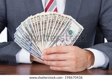 Midsection of businessman holding fanned banknotes at desk