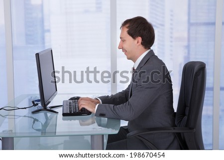 Side view of mid adult businessman working on computer at desk in office