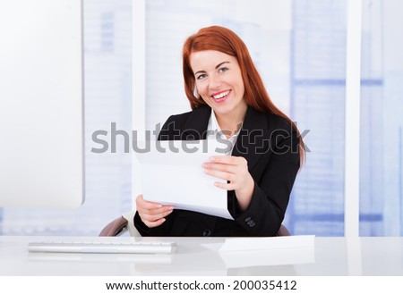 Portrait of happy businesswoman holding document at office desk