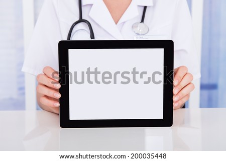 Midsection of female doctor displaying digital tablet at desk in hospital