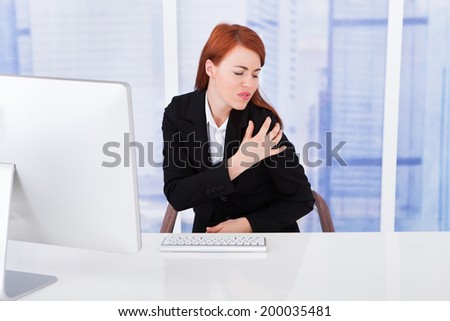 Young businesswoman having shoulder pain while working at computer desk in office