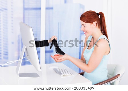 Side view of young businesswoman shopping shoes online at computer desk