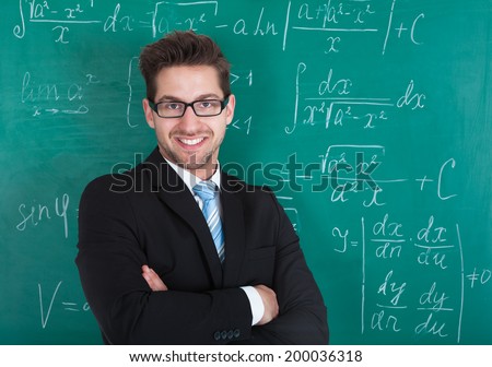 Portrait of confident young male professor standing against blackboard in classroom