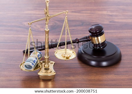 Judge gavel and scales with money on wooden desk