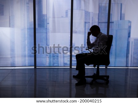 Full length side view of tensed businessman sitting on chair by office window