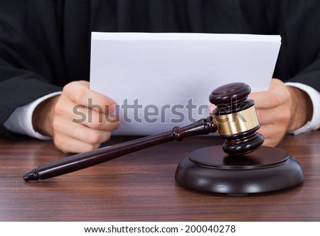 Closeup of gavel placed on block with judge reading documents at desk