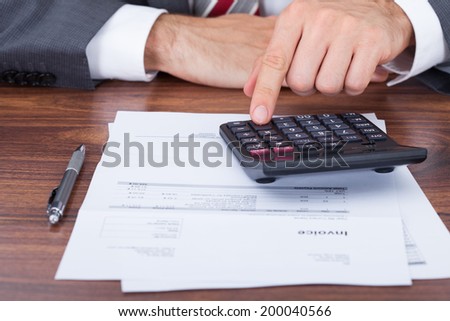 Midsection of businessman using calculator on invoice documents at office desk