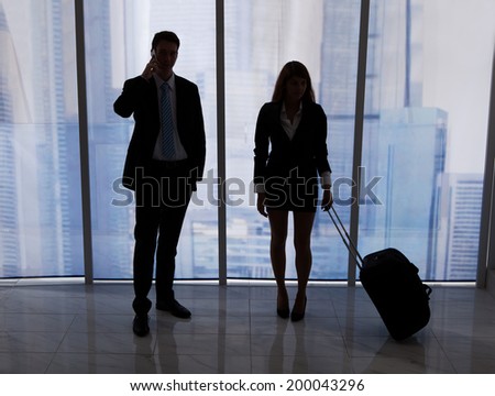 Full length of young businessman on call standing by female colleague with luggage in office
