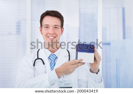 Portrait of confident young male doctor holding medicine box in hospital