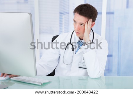 Worried young male doctor using computer at desk in hospital