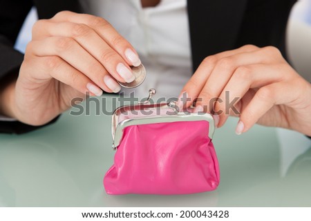 Midsection of businesswoman putting coin into pink purse at office desk