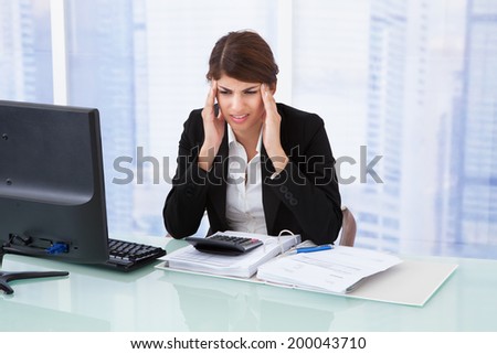 Stressed young businesswoman suffering from headache at computer desk in office