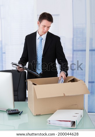 Young businessman collecting office supply in cardboard box at office desk