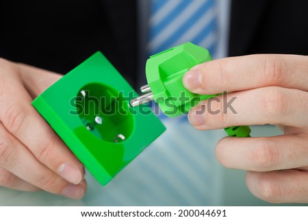 Cropped image of businessman holding green electric plug and socket at office desk
