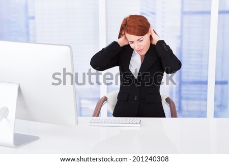 Young businesswoman having neck pain while working at computer desk in office
