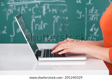 Cropped image of female university student using laptop in classroom