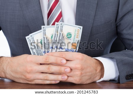 Midsection of businessman holding fanned banknotes at desk