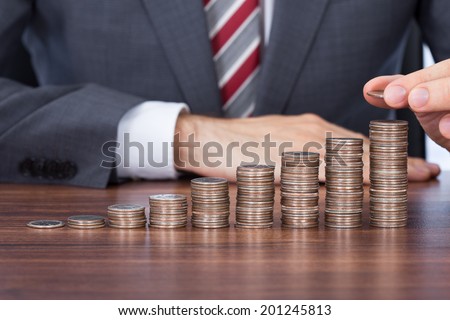 Midsection of businessman stacking coins in increasing order at desk