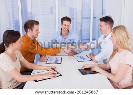 Two businessmen shaking hands in front of colleagues during conference meeting