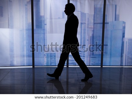 Full length side view of businessman walking by office window with city view in background