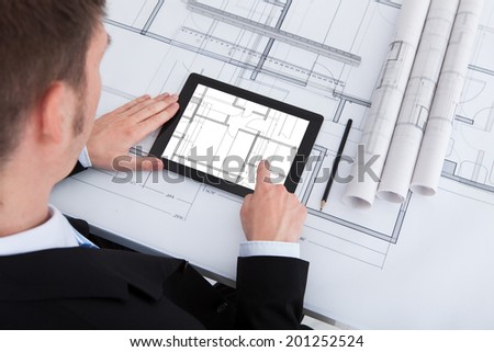 High angle view of male architect using digital tablet on blueprint in office
