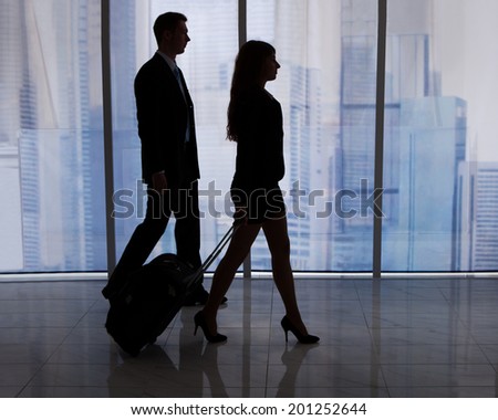 Full length of young businessman and businesswoman walking with luggage in office