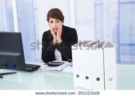 Worried businesswoman looking at binders on office desk