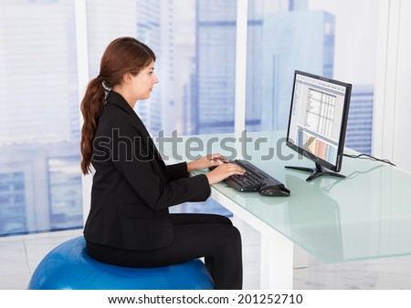 Side view of businesswoman using computer while sitting on fitness ball at desk in office