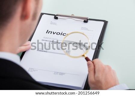 Cropped image of young businessman examining invoice through magnifying glass at office desk