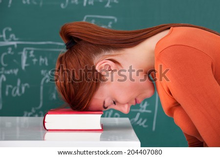 Side view of sad young female student leaning head on book in classroom