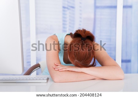 Tired young businesswoman sleeping at computer desk in office