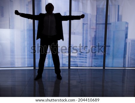 Full length rear view of businessman standing arms outstretched by office window