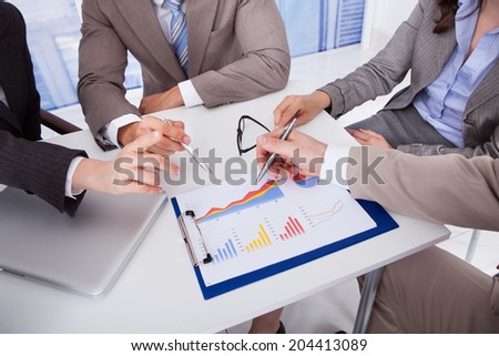 Midsection of business people discussing over graph at table in office
