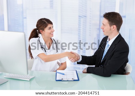 Young female doctor greeting businessman at desk in clinic