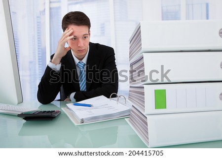 Worried businessman looking at stacked binders on office desk