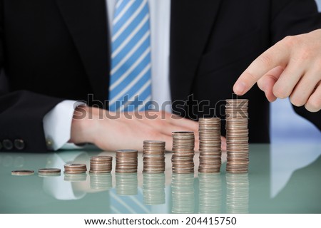 Midsection of young businessman with coins stacked as bar graph at office table